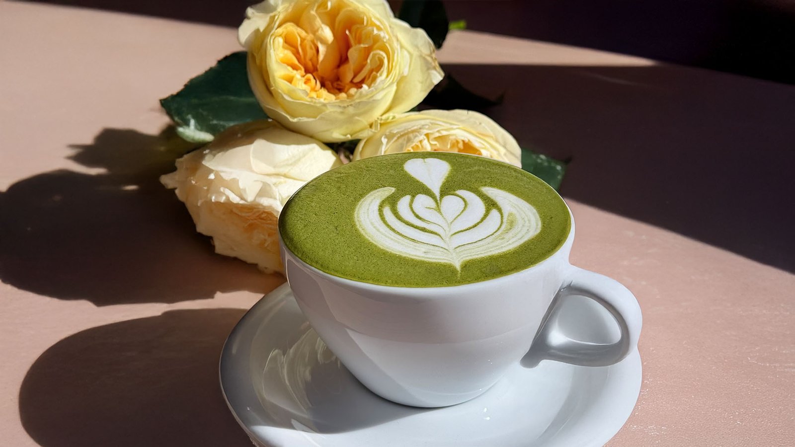 Matcha latte art beside yellow garden roses